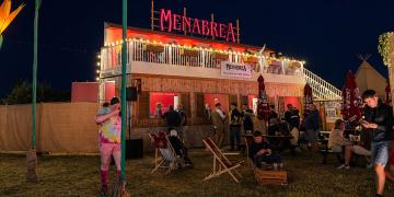 shipping container bar at night with illuminated branding and upper deck 